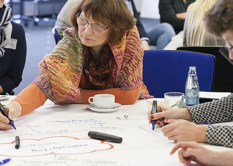 Personen schreiben auf das Papier eines Worldcafé-Tischs
